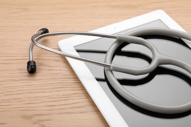 Photo of Computer tablet with stethoscope on wooden table, closeup