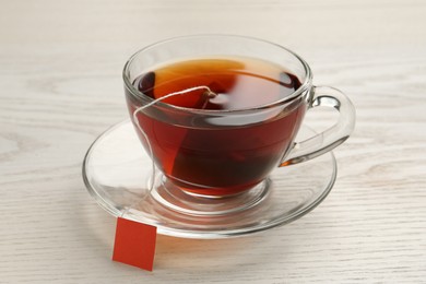 Tea bag in glass cup of hot water on white wooden table, closeup