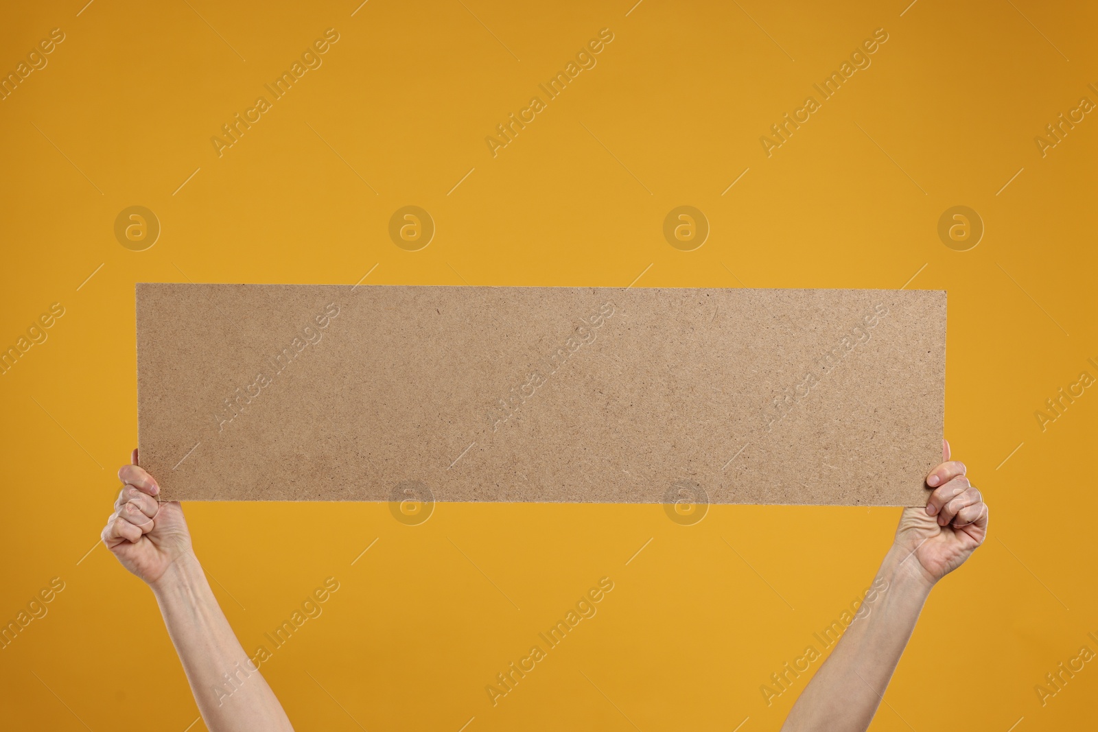 Photo of Woman holding blank cardboard banner on orange background, closeup. Space for text