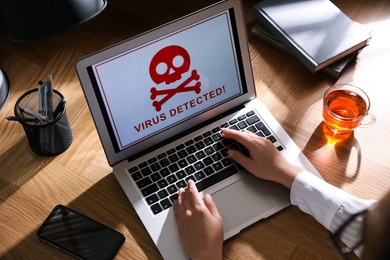 Photo of Woman using laptop with warning about virus attack at workplace, closeup
