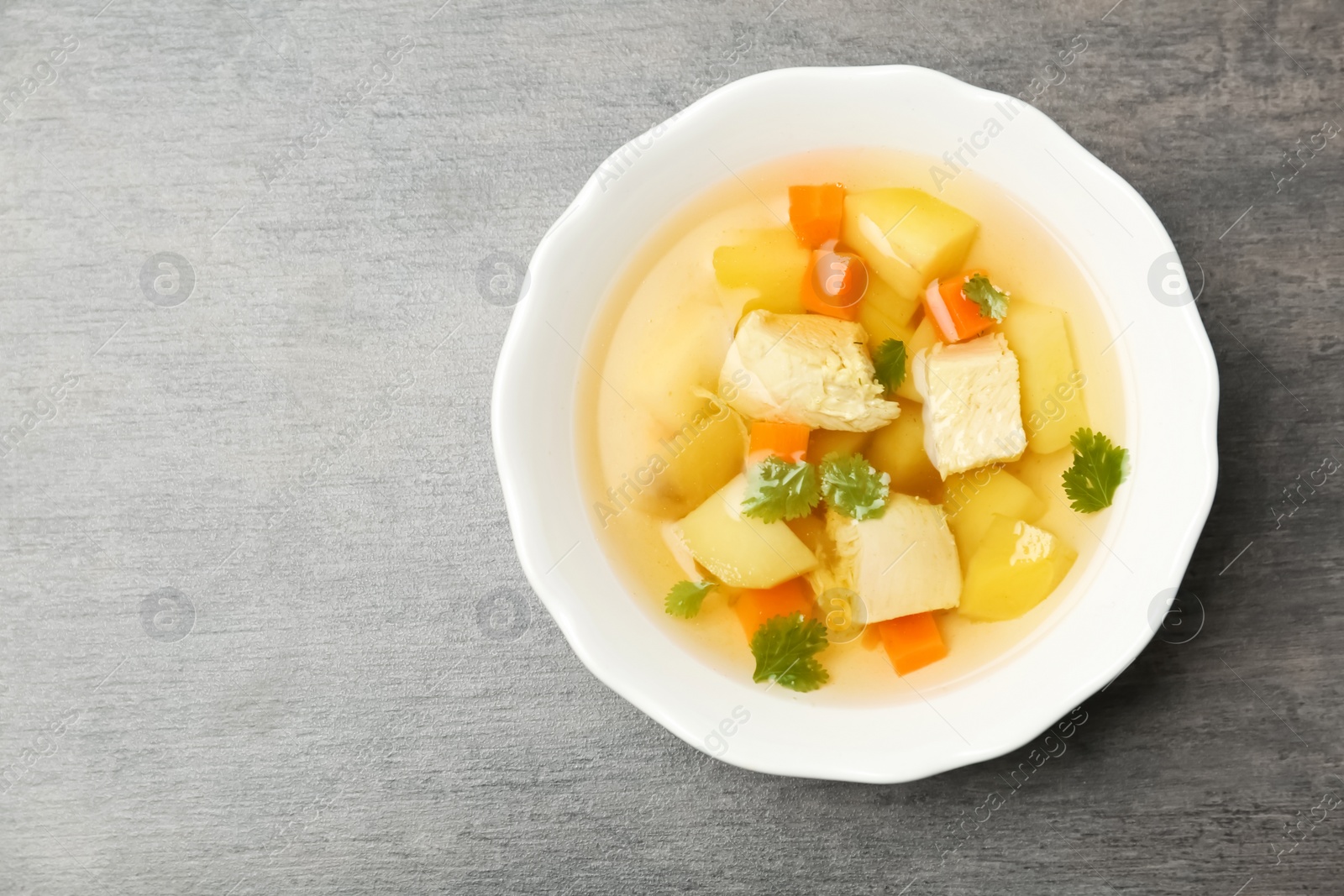 Photo of Homemade chicken soup in dish on grey background, top view with space for text