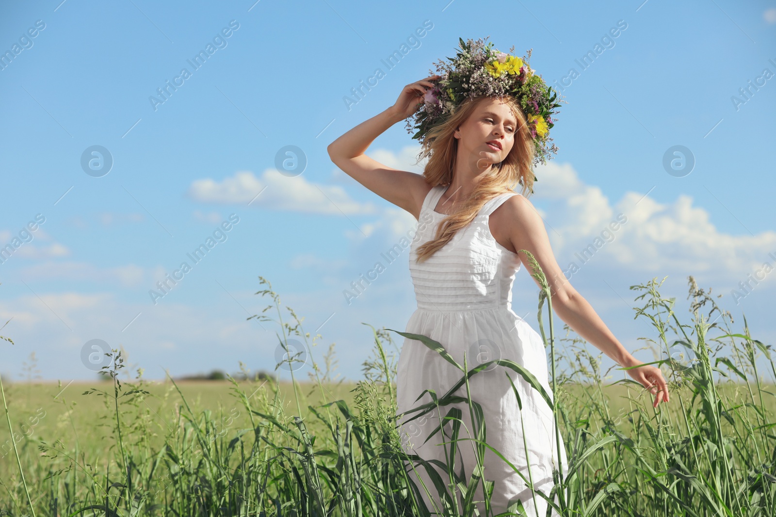 Photo of Young woman wearing wreath made of beautiful flowers in field on sunny day