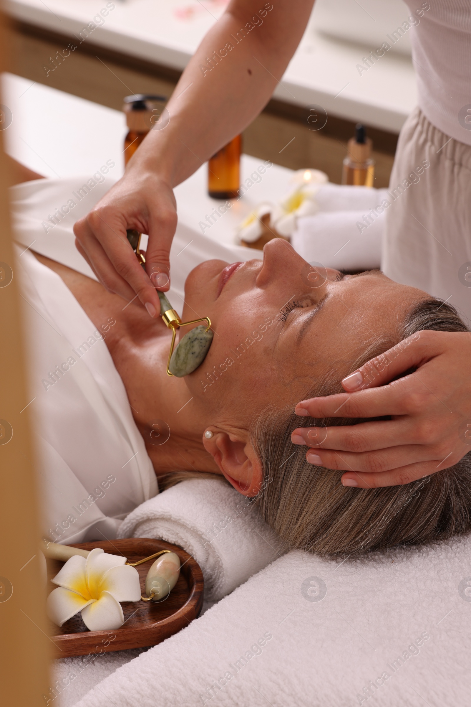 Photo of Woman receiving facial massage with jade roller in beauty salon, closeup