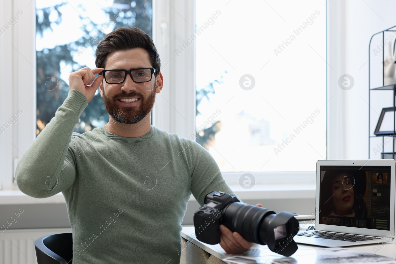 Photo of Professional photographer in glasses holding digital camera at table in office