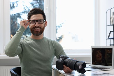Photo of Professional photographer in glasses holding digital camera at table in office