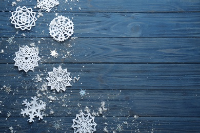 Flat lay composition with paper snowflakes on blue wooden background, space for text. Winter season
