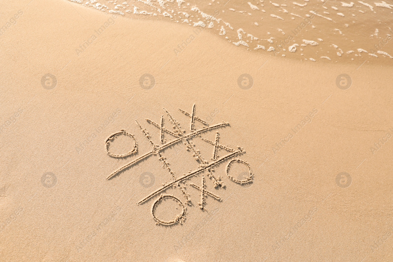 Photo of Tic tac toe game drawn on sand near sea, above view