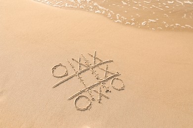 Tic tac toe game drawn on sand near sea, above view