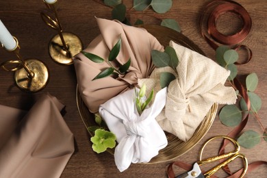 Photo of Furoshiki technique. Flat lay composition with gifts packed in different fabrics and flowers on wooden table