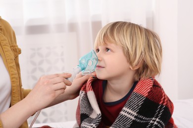 Mother helping her sick son with nebulizer inhalation at home