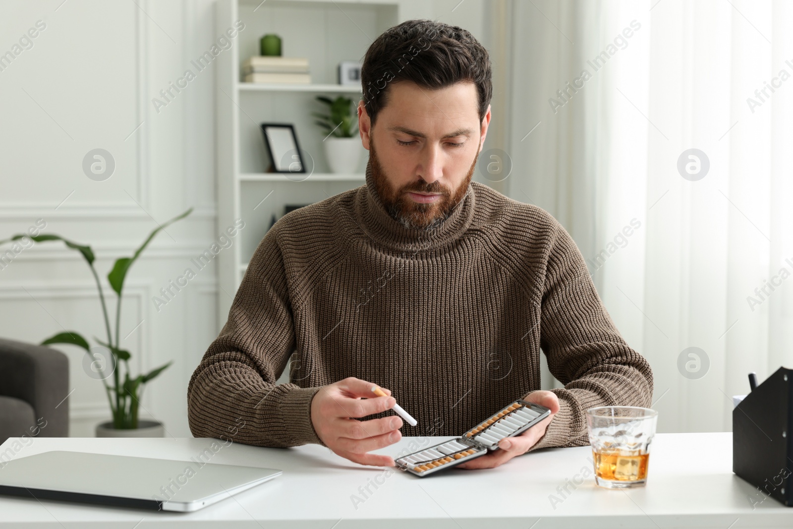 Photo of Man taking cigarette from case at white table in office