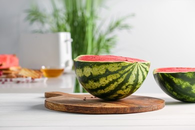 Photo of Halves of delicious ripe watermelon on white wooden table in kitchen, space for text