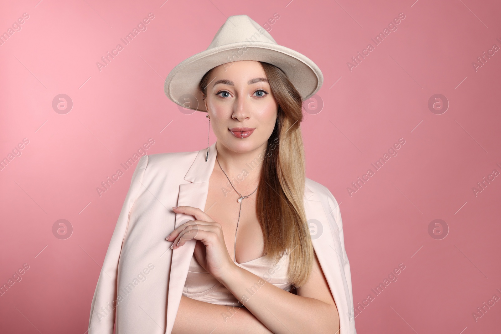 Photo of Young woman with lip and ear piercings on pink background