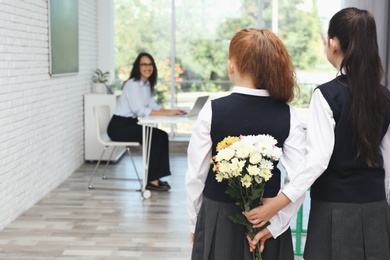 Photo of Schoolgirls with bouquet congratulating their pedagogue in classroom. Teacher's day