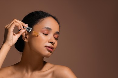 Photo of Beautiful woman applying serum onto her face on brown background. Space for text