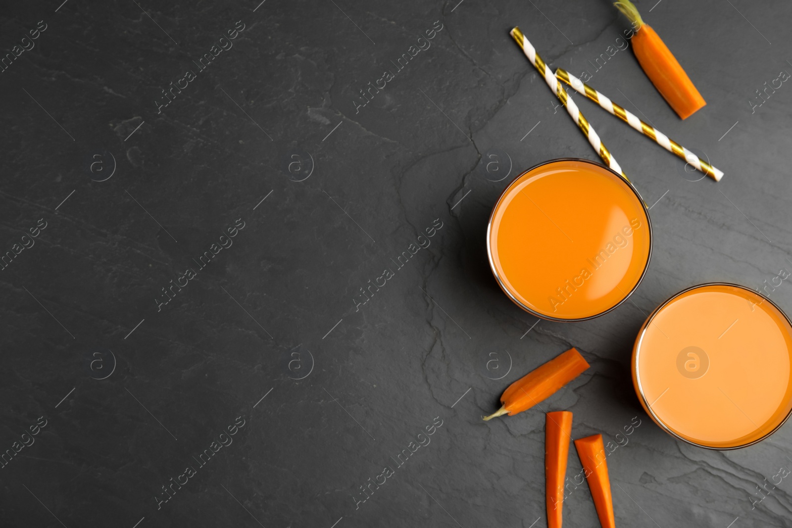 Photo of Glasses of freshly made carrot juice on black table, flat lay. Space for text