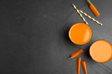 Photo of Glasses of freshly made carrot juice on black table, flat lay. Space for text