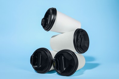 Photo of White paper cups with black lids on light blue background. Coffee to go