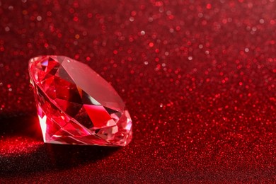 Photo of Beautiful shiny diamond on red glitter background, closeup. Space for text