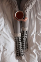 Woman with cup of tea on soft blanket, top view