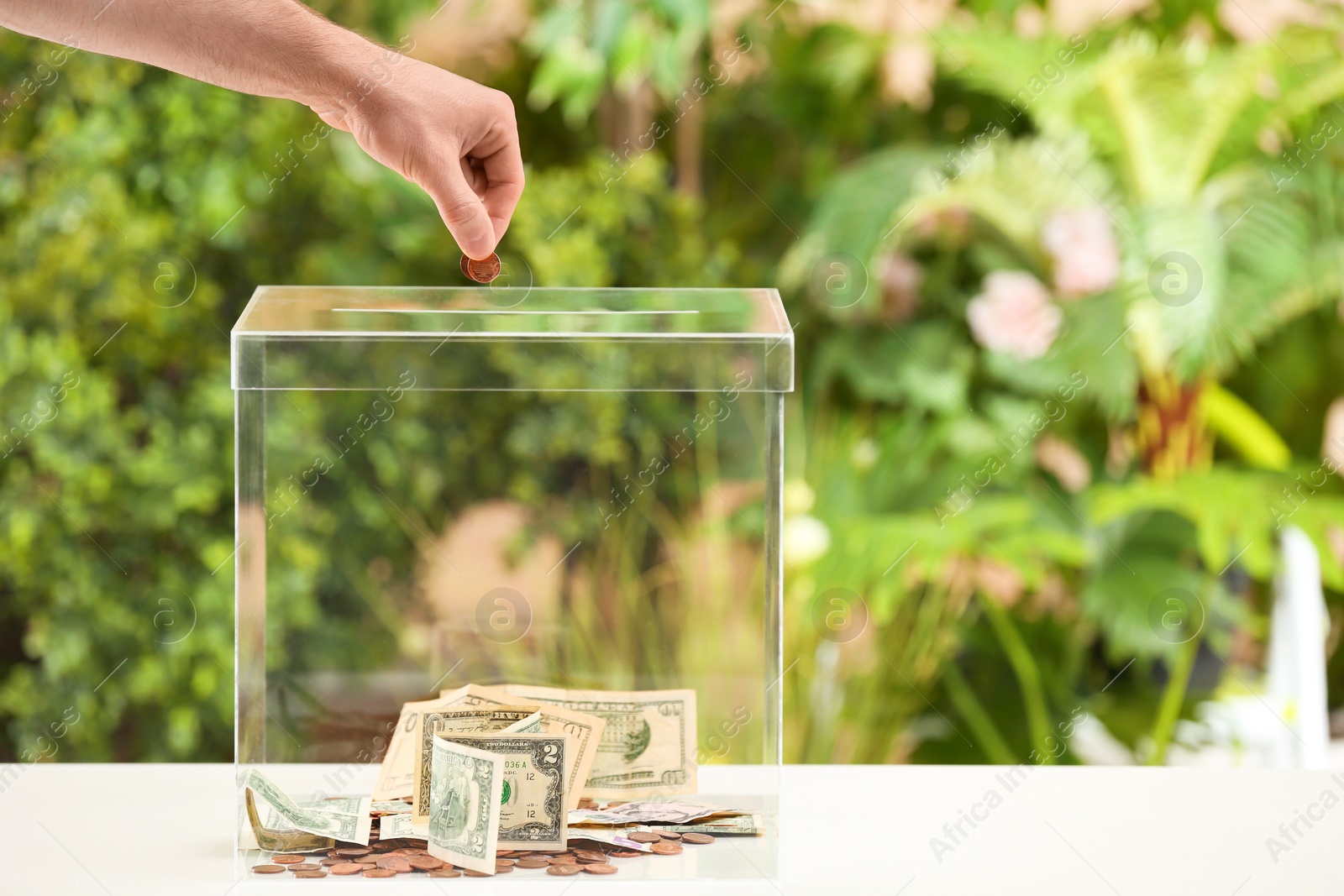 Photo of Man putting coins into donation box on table against blurred background, closeup. Space for text