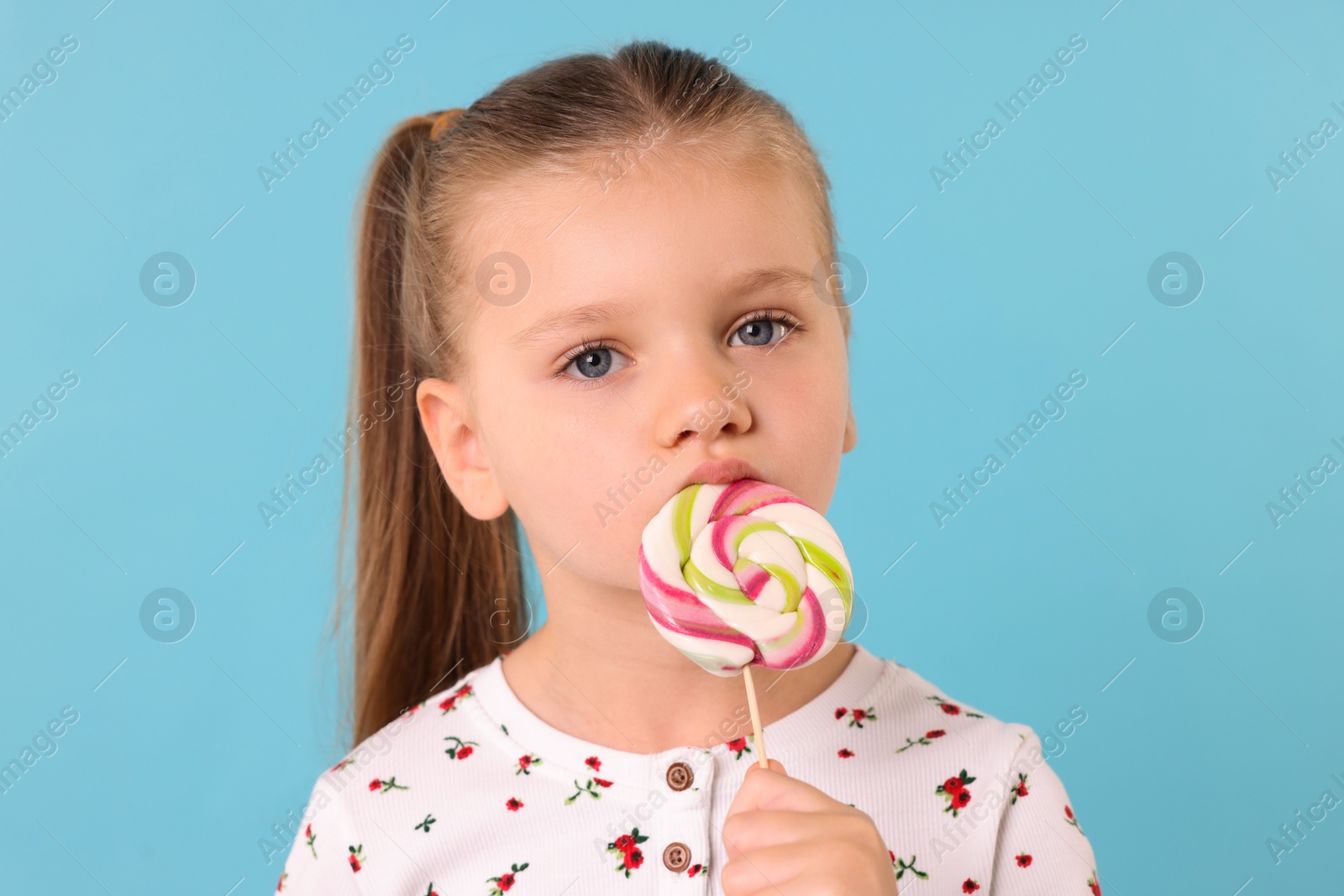 Photo of Cute little girl licking colorful lollipop swirl on light blue background