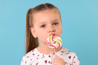 Cute little girl licking colorful lollipop swirl on light blue background