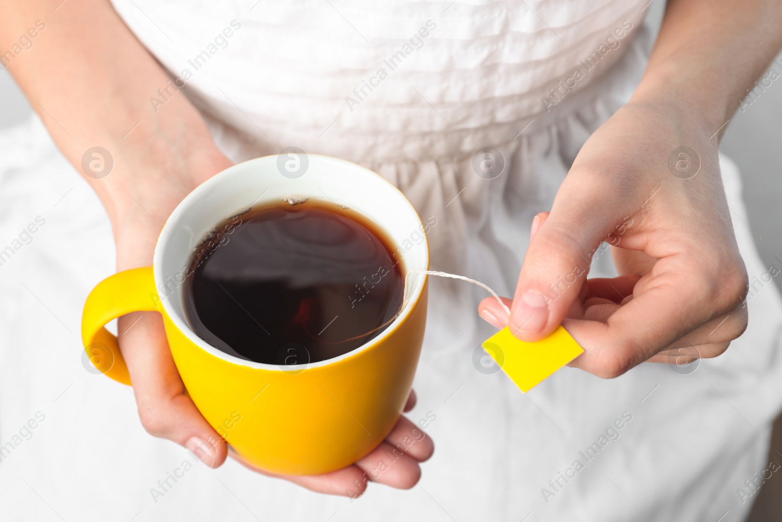 Photo of Woman taking tea bag out of cup with beverage, closeup