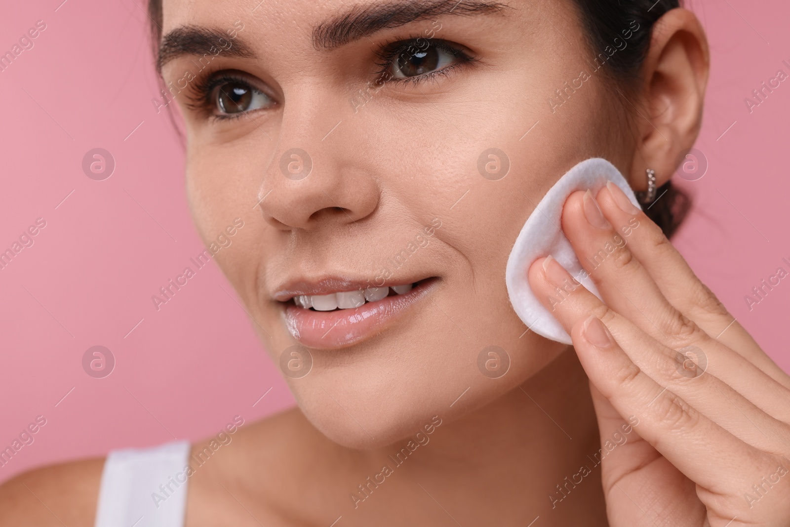 Photo of Young woman cleaning her face with cotton pad on pink background, closeup