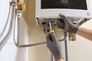 Man repairing gas boiler with screwdriver indoors, closeup