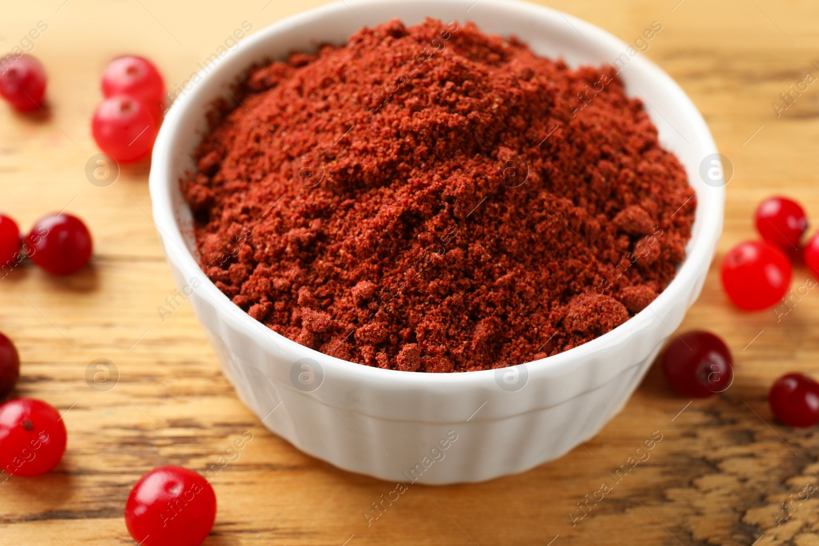 Photo of Dried cranberry powder in bowl and fresh berries on wooden table, closeup