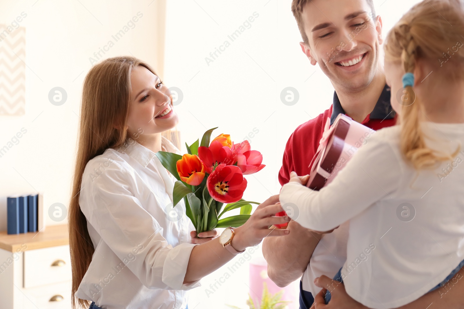 Photo of Happy woman receiving flowers and gift from her family at home. Mother's day celebration