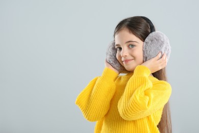 Photo of Cute girl wearing stylish earmuffs on grey background. Space for text