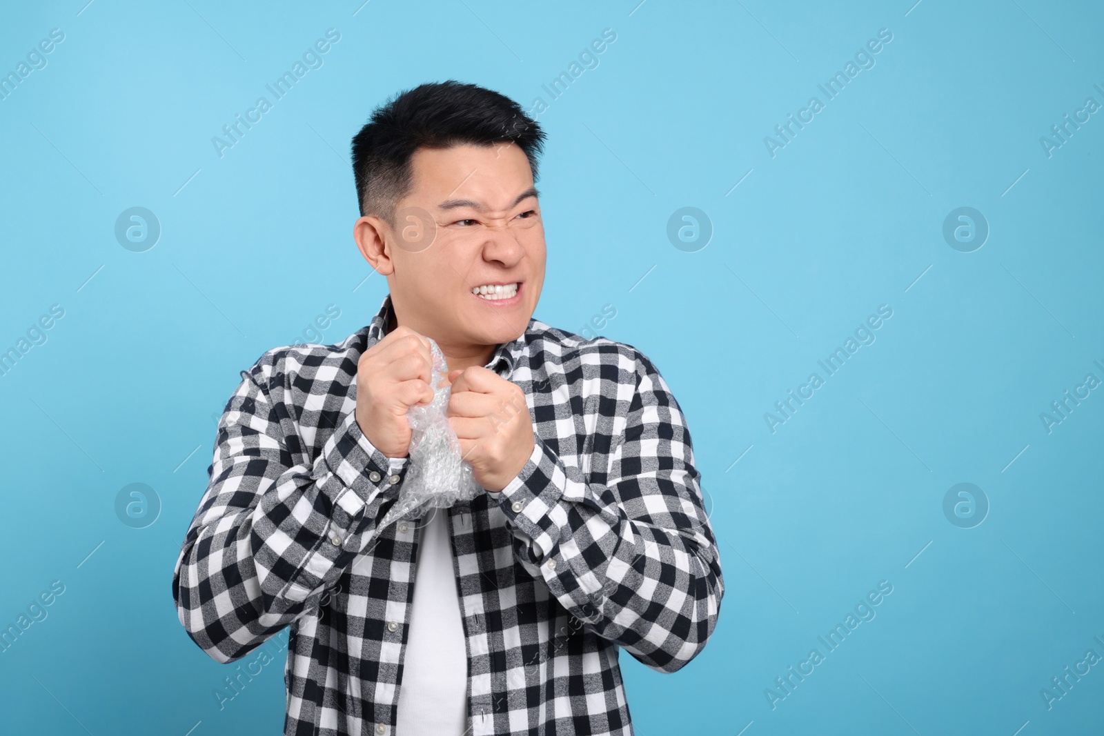 Photo of Emotional asian man with bubble wrap on light blue background. Space for text