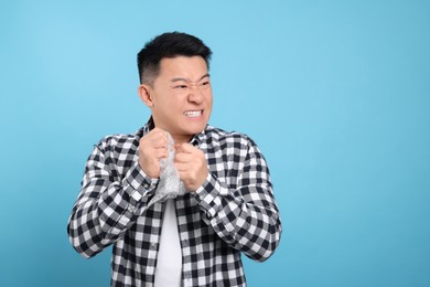 Photo of Emotional asian man with bubble wrap on light blue background. Space for text