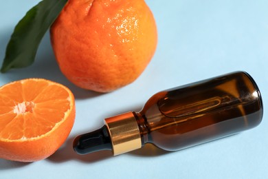 Photo of Aromatic tangerine essential oil in bottle and citrus fruits on light blue table, closeup