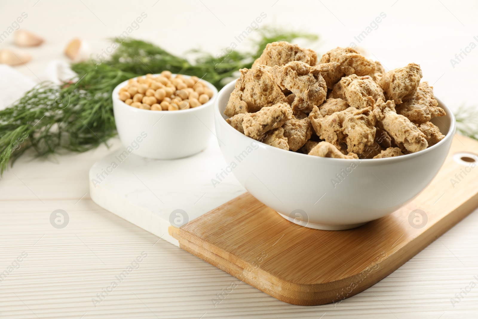 Photo of Dried soy meat in bowl on white wooden table, space for text