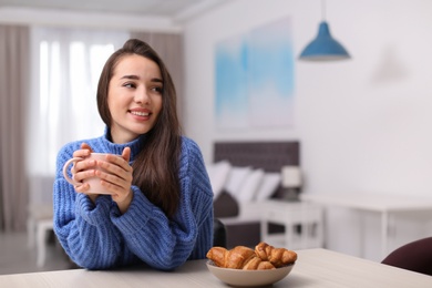 Photo of Young woman drinking coffee at table indoors, space for text. Winter season