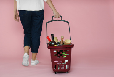 Photo of Woman with shopping basket full of different products on pink background, closeup