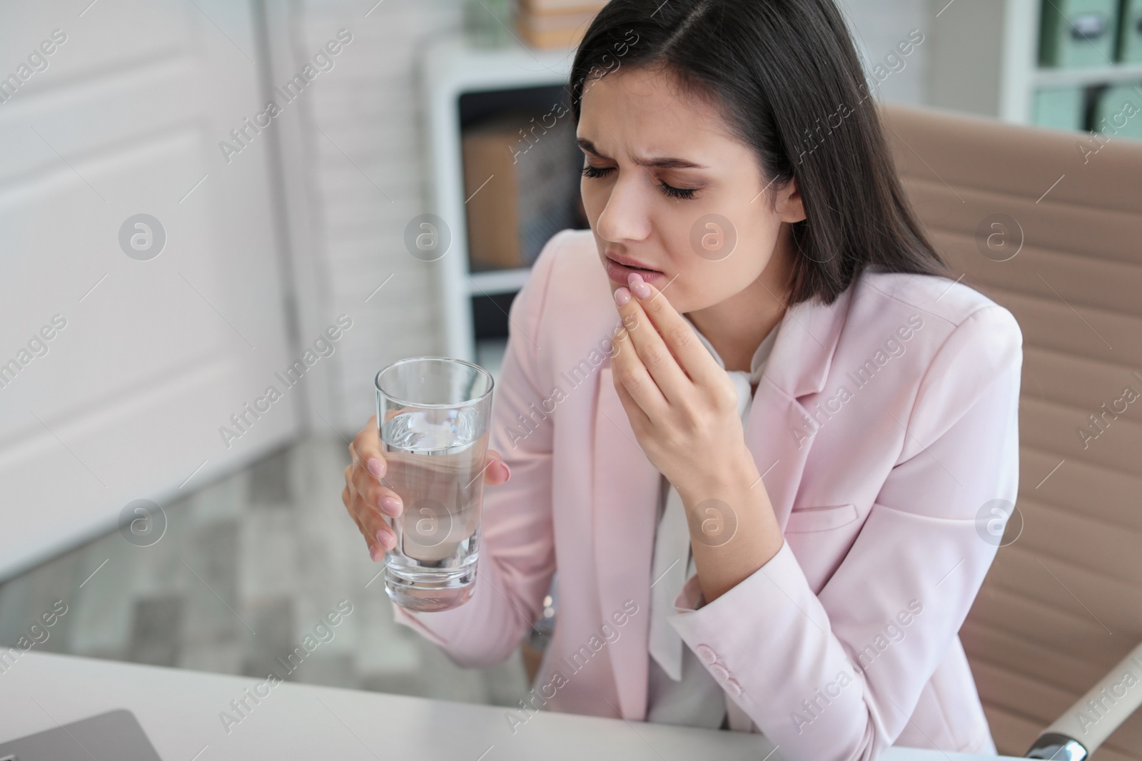 Photo of Young woman taking pill against headaches while sitting at table in office