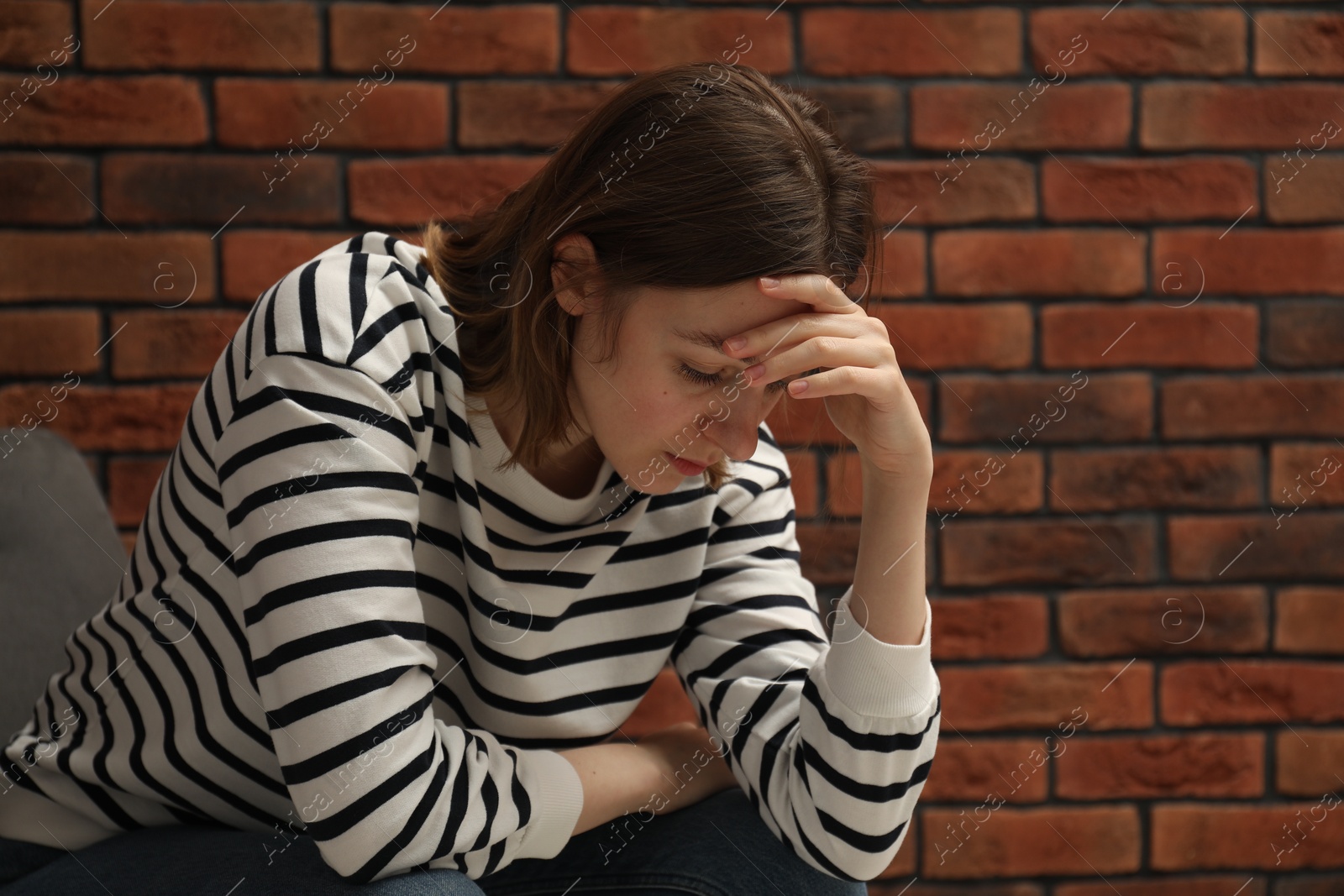 Photo of Sad young woman sitting on chair near brick wall, space for text