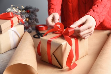 Photo of Christmas present. Woman tying ribbon bow on gift box at table, closeup