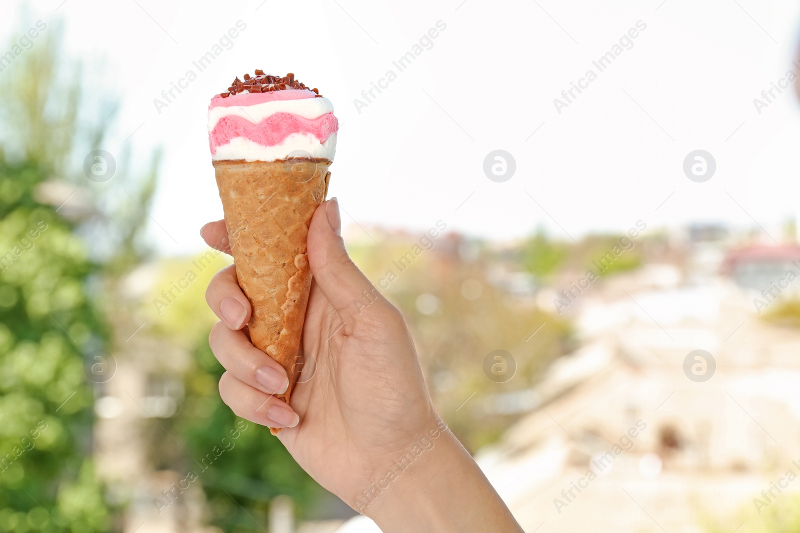 Photo of Woman holding yummy ice cream on blurred background. Focus on hand