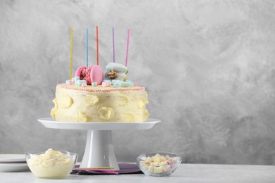 Photo of Delicious cake decorated with macarons, marshmallows and candles served on white table against grey background, space for text