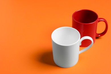 Photo of Red and white ceramic mugs on orange background, space for text