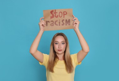 Photo of Young woman holding sign with phrase Stop Racism on light blue background