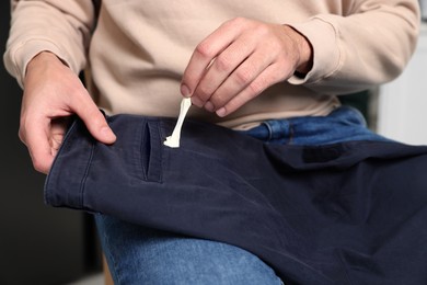Photo of Man removing chewing gum from black jeans, closeup