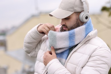 Photo of Handsome man in warm scarf and headphones on blurred background