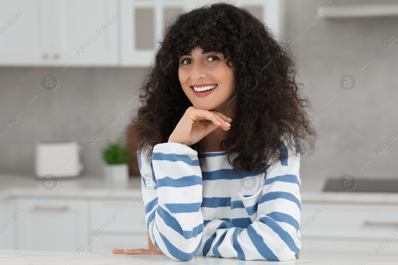 Photo of Portrait of beautiful woman with curly hair in kitchen. Attractive lady smiling and looking into camera