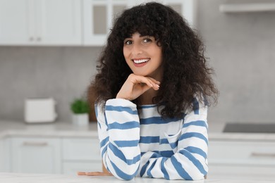 Portrait of beautiful woman with curly hair in kitchen. Attractive lady smiling and looking into camera